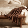 Beige pom pom knit throw on a walnut bench at the foot of a bed