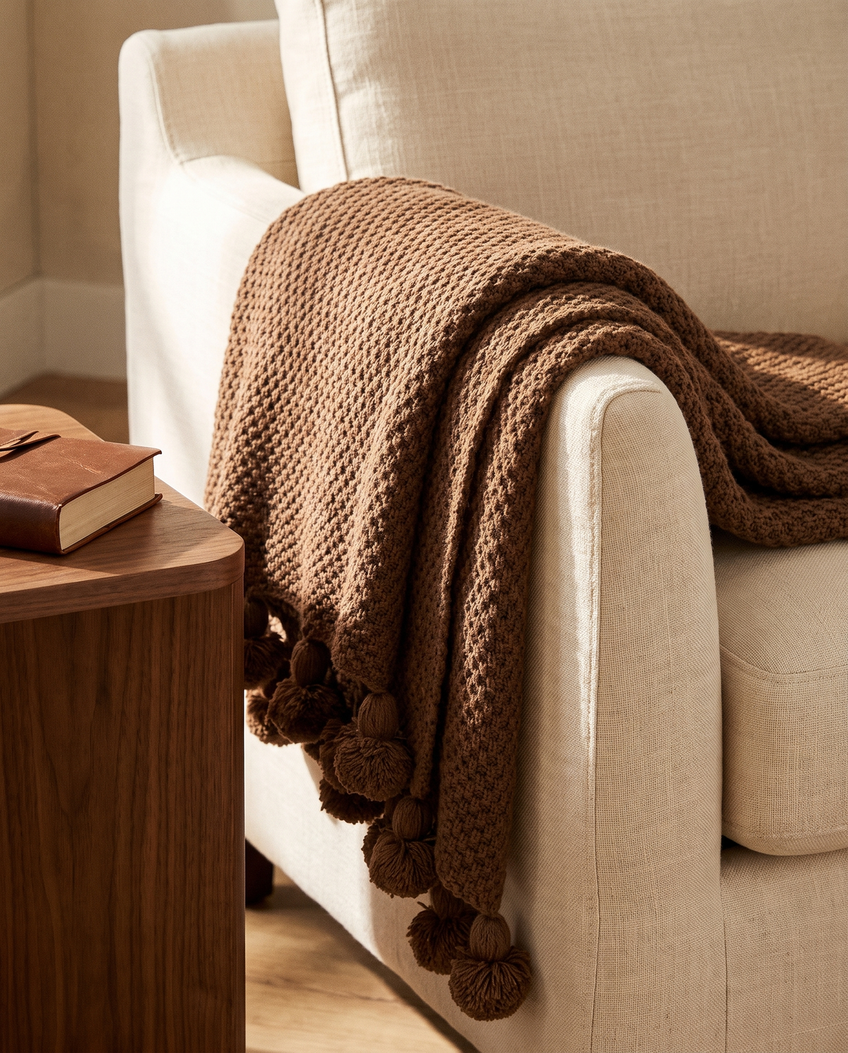 Pom pom knit throw folded over a cream armchair